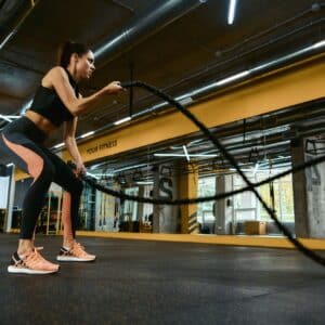Cardio workout. Young strong athletic woman wearing sport clothes exercising with battle ropes at