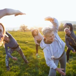 Seniors with sport instructor doing exercise outdoors in nature at sunset, active lifestyle.